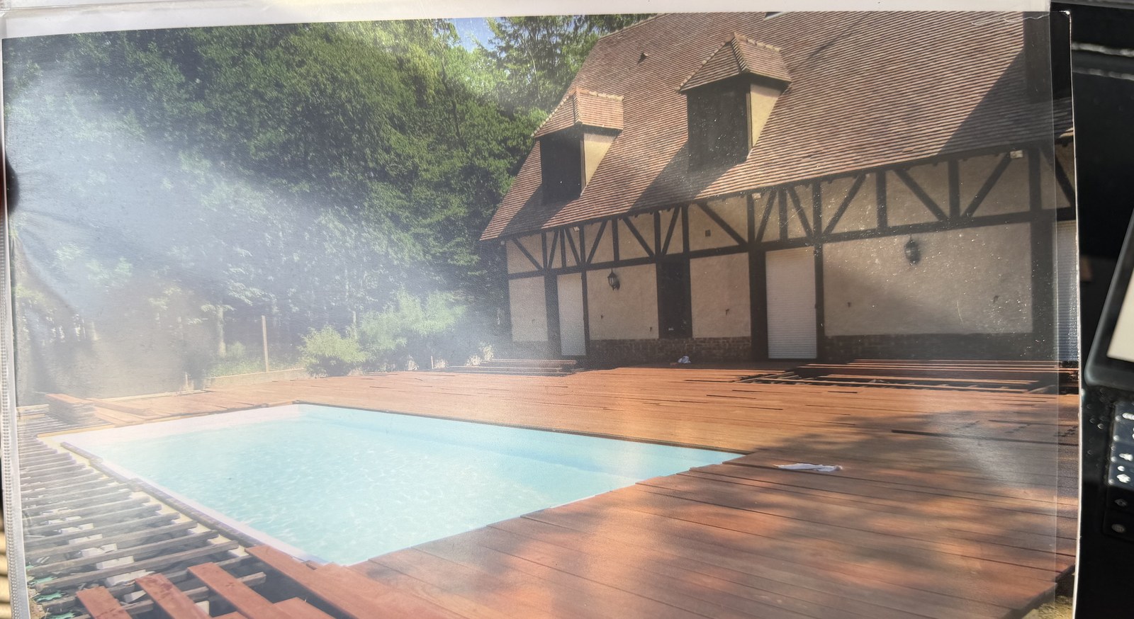 Piscine bordée d'une terrasse en ipé devant une maison normande à colombages